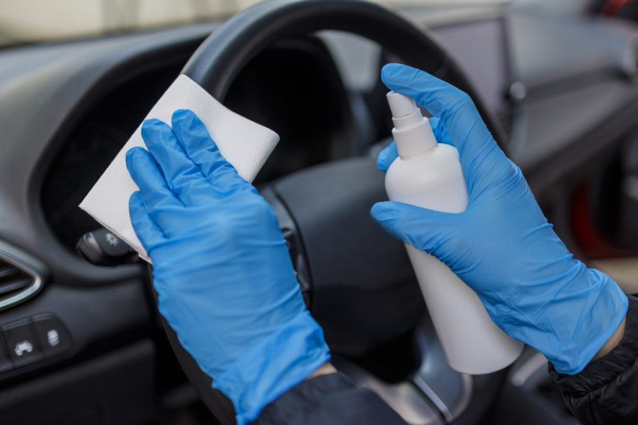 Woman in protective gloves spraying and wiping steering wheel of a car