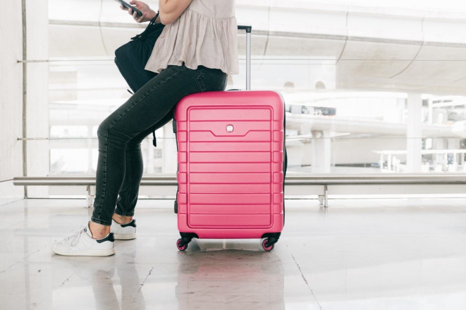Woman sitting on pink luggage waiting for Land to Air shuttle service.