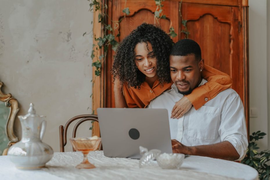 A woman with her arm around her husband looking at laptop.