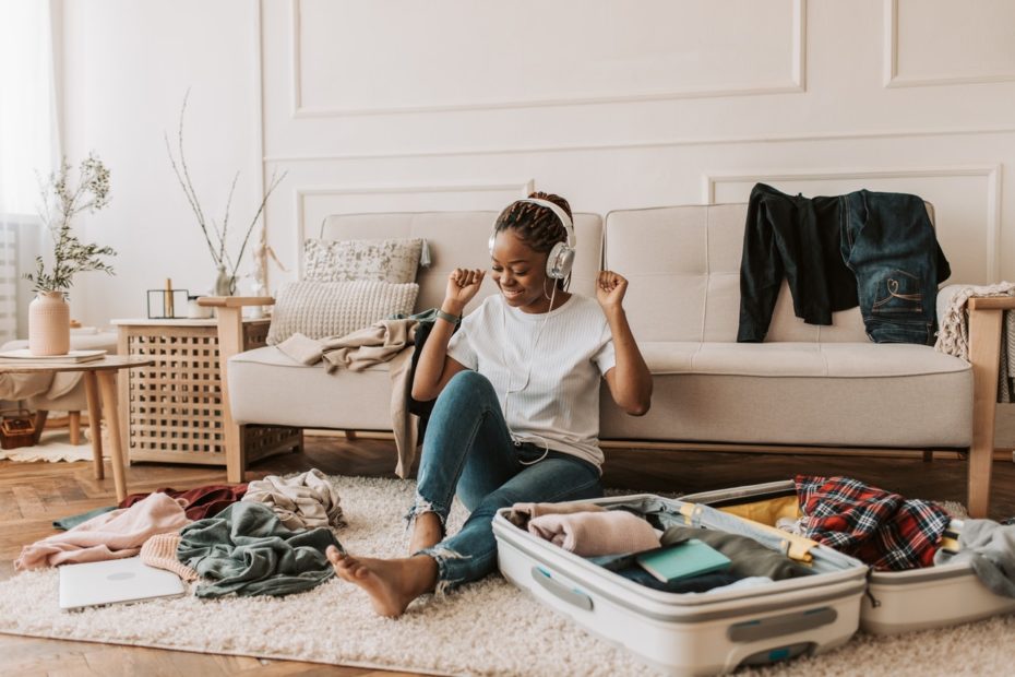 Young female traveler sitting on floor with suitcase listening to music.