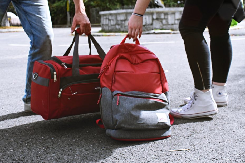 A man and woman picking up their carry-on luggage from road.