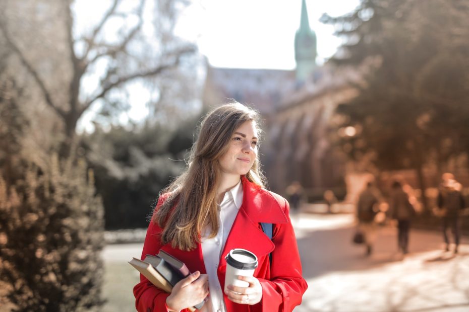 Young college student walking on campus with books and coffee.